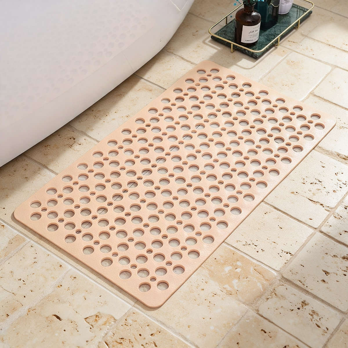 Beige Secure Shower Mat laid on travertine tile beside a bath, drainage holes visible