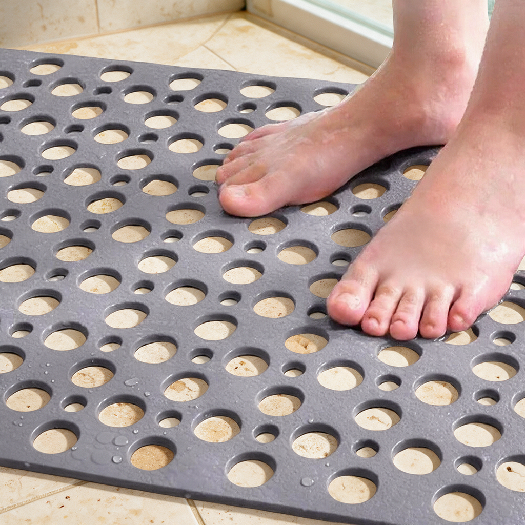 Bare feet standing on the grey Secure Shower Mat over warm travertine tile, water draining through the holes