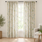 Wildflower Veil Curtain, cream linen-look fabric with blue and green botanical leaf print and tassel trim, two panels floor-length at a tall window in a bright living room
