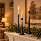 Three black iron candlesticks with lit tapers on a white fireplace mantel with greenery