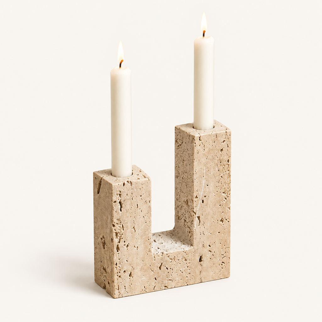 Dual travertine sculpted candle holder with two lit ivory taper candles on a warm off-white background