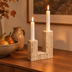 Travertine taper candle holder lit on a dining room sideboard beside a bowl of pears