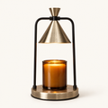 Melté candle warmer lamp in Champagne Noir, brass cone shade and black frame, warming an amber jar candle