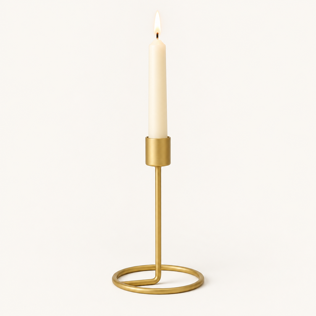 Small gold taper candlestick with a lit ivory taper candle on a warm off-white background