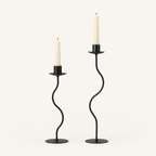 Sculpted wavy iron candle holders in matte black, small and large, with lit taper candles