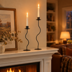 Pair of wavy black taper candle holders lit on a white fireplace mantel on an autumn evening