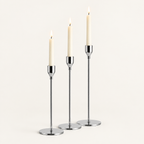 Set of 3 silver taper candlesticks in graduated heights with lit ivory candles