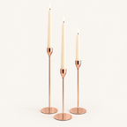 Set of 3 rose gold taper candlesticks in graduated heights with lit ivory candles