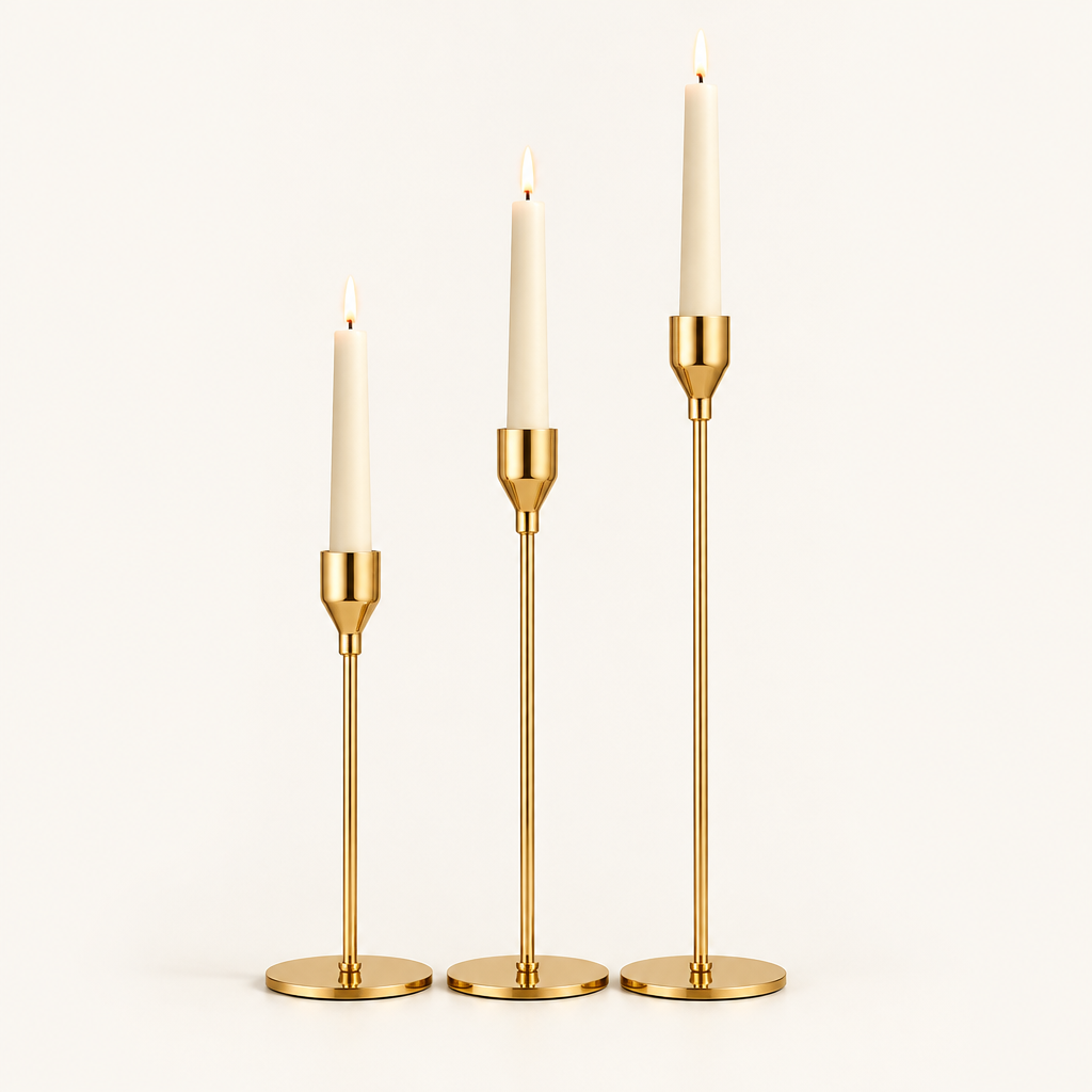 Set of 3 gold taper candlesticks in graduated heights with lit ivory candles on a warm off-white background