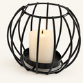 Sculptural Black rounded wire candle holder with a lit pillar candle on a warm off-white background