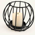 Sculptural Black rounded wire candle holder with a lit pillar candle on a warm off-white background