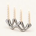 Cosmic Ripple silver ceramic wave candelabra holding four lit twisted taper candles