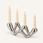 Cosmic Ripple silver ceramic wave candelabra holding four lit twisted taper candles