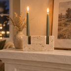 Travertine candle holder with sage green tapers on a plaster fireplace mantel