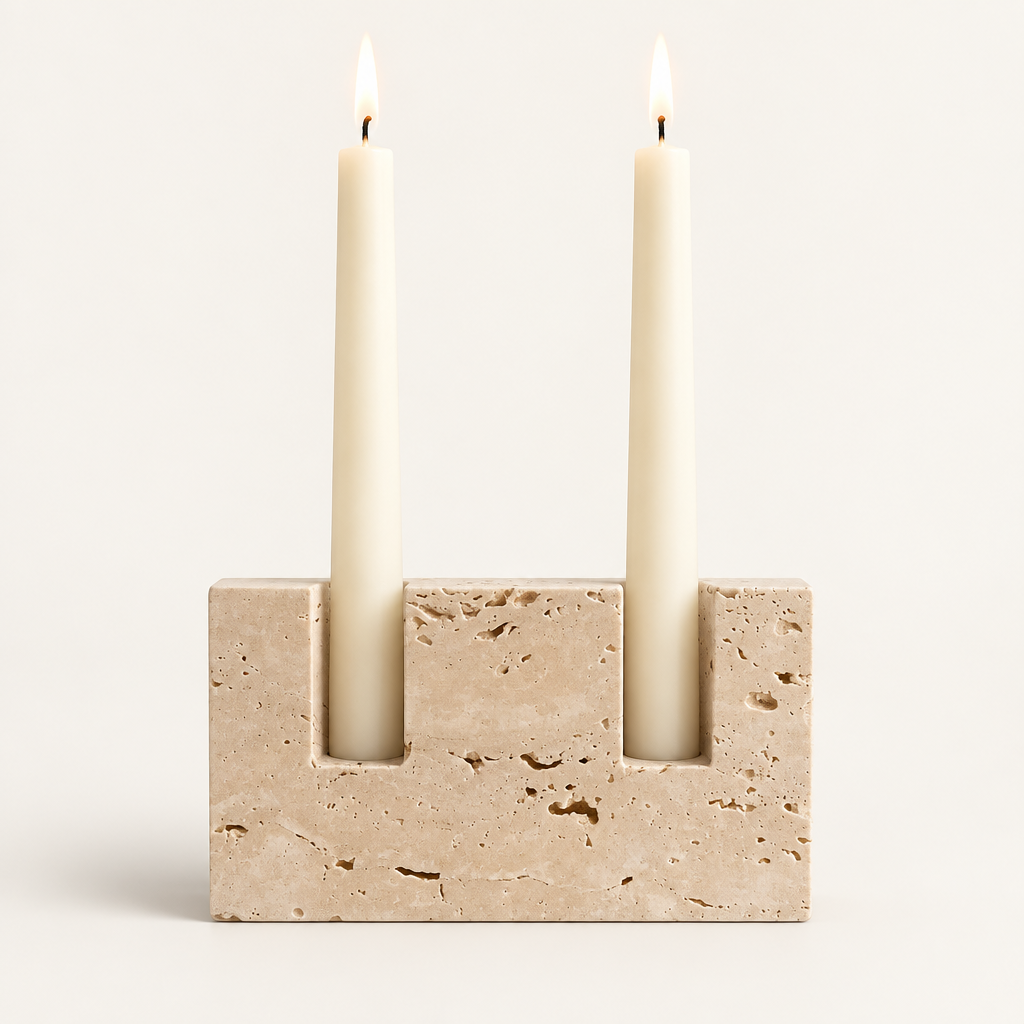 Dual travertine taper candle holder with two lit ivory tapers on a warm off-white background