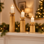 Carved wooden candle holders on a fireplace mantel with a pine garland