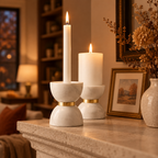 Marble hourglass candle holders lit on a stone fireplace mantel on an autumn evening