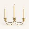 Gilded Trio gold iron 3-candle taper holder with three lit ivory candles on a warm off-white background