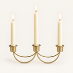 Gilded Trio gold iron 3-candle taper holder with three lit ivory candles on a warm off-white background
