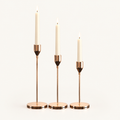 Set of 3 rose gold metal taper candle holders with lit ivory taper candles