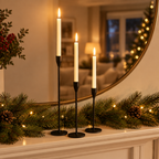 Black taper candle holders on a fireplace mantel with a pine garland and round mirror